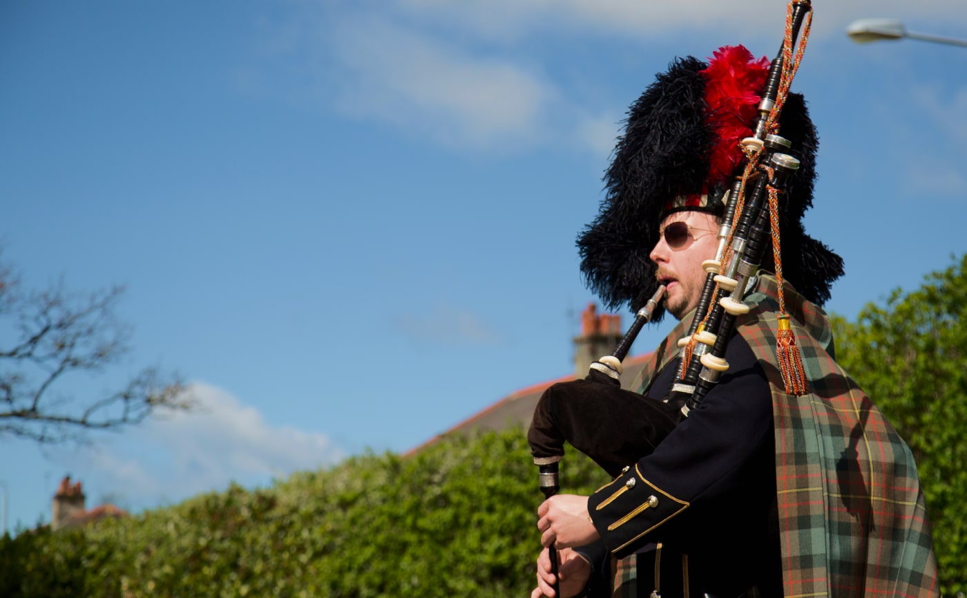 Medium close shot of piper (Philip Barlow) playing bagpipes